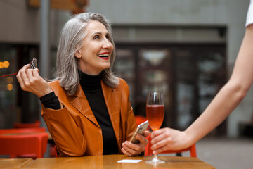 Grey white senior woman using mobile phone while drinking wine in cafe