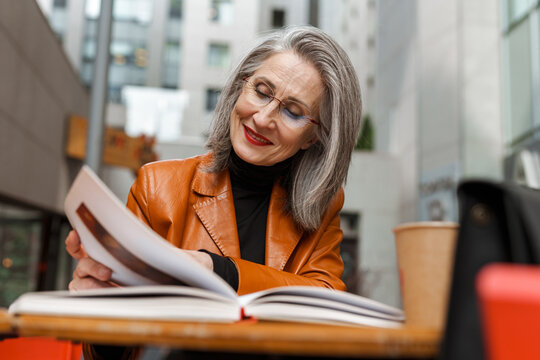 Grey white senior woman reading book while sitting in cafe
