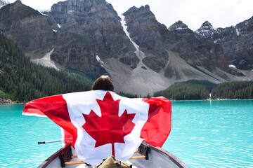 Young girl in a canoe holding canadian flag, surrounded by turqouise lake and mountains