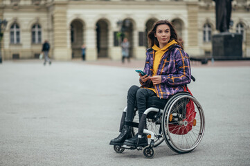 Fototapeta na wymiar Woman in wheelchair using a smartphone while out in the city