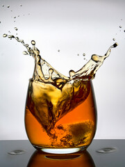 Creative splashes of whisky in a glass against a white background. 