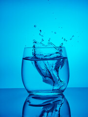 Creative splashing water in the glass on blue background. 