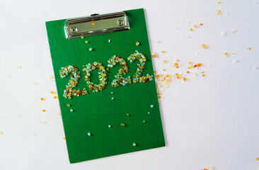 New Year 2022 on a green tablet with colored beads and fir branches on the background of the workspace. The concept of the beginning of success and the idea of a business task