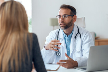 Shot of handsome mature male doctor talking while explaining medical treatment to patient in the...