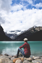 Woman in red plaid shirt sitting on rocks admiring the view of lake and mountains