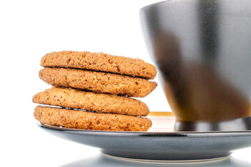 Four fresh oatmeal cookies on a black ceramic saucer with a cup, close-up, isolated on white.