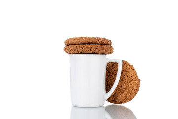 Three fresh oatmeal cookies with a white ceramic cup, close-up, isolated on white.