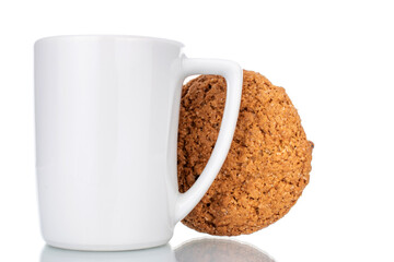 One fresh oatmeal cookie with a white ceramic cup, close-up, isolated on white.