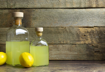 Two bottles with limoncello and lemons with copy space on wooden background