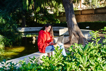 Naklejka na ściany i meble college student girl sitting in the park working with laptop