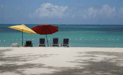 Tropical secluded beach with red and yellow umbrellas and chairs overlooking the ocean