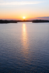 Bright colorful sunset over the Daugava river. The sun sets low above the horizon in a beautiful cloud, and is reflected on the surface of the water. Natural landscape