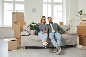 Portrait of happy young family in new home. Smiling married couple sitting on cozy comfortable sofa...