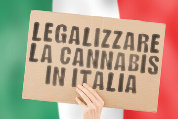 The phrase " Legalizzare la cannabis in Italia " on a banner in men's hand with blurred Italian flag on the background. Addictive. Medication. Problem. Dependence. Decriminalisation