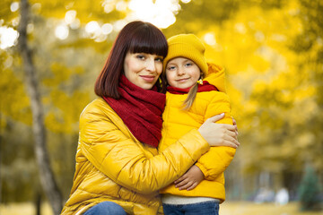 Family outdoor portrait. Happy autumn together. Lovely mother and adorable little daughter in autumn yellow park, hugging and smiling at camera
