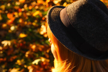 Closeup back portrait of candid young Caucasian blonde woman in colorful autumn park. Bright dark stylish woman in hat and shawl of neck on fall background. Happy fall dreaming waiting concept