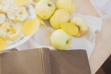 Yellow apples and baked apples lie on a plate near an open book in autumn with autumn leaves