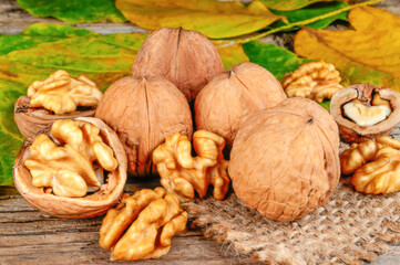 fresh kernels, broken and whole walnuts close-up on wooden background with yellow fall leafs