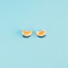 Creative arrangement made of tangerines and eyelashes on a blue background. Minimal eyelid concept. Sleep and autumn inspiration.