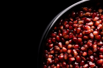 A lot of beautiful red pomegranate seeds in a black bowl