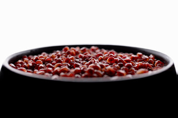A lot of beautiful red pomegranate seeds in a black bowl on a white background
