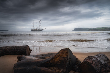 Dramatic storm sky rolling over anchored tall ship near Northern Ireland coast, Fair Head in far...