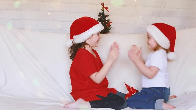 Smiling little girls in a Santa Claus hat are having fun doing dance moves in anticipation of the New Year and Christmas. Blurred bokeh background