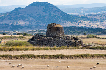 Stunning landscape with the ancient Santu Antine Nuraghe and some sheep grazing in the foreground. Santu Antine Nuraghe is one of the largest Nuraghi in Sardinia, Italy. - obrazy, fototapety, plakaty