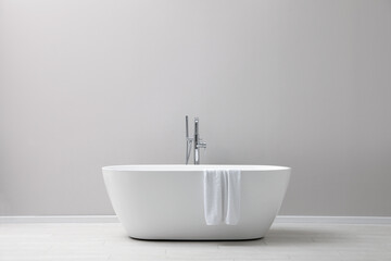 Naklejka na ściany i meble Modern ceramic bathtub with towel near light wall indoors