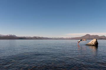 Child enjoying summer, jumping from a stone to the lake.