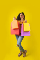 Mujer afroamericana de pie alegre sosteniendo unas bolsas de compra en un fondo amarillo