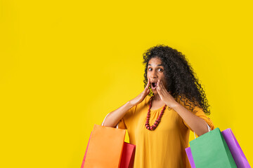 Mujer afroamericana con gesto de asombro en fondo amarillo con bolsas de compra