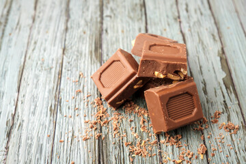 Various Pieces of chocolate with peanuts stacked frontally on a wooden background accompanied by grated chocolate
