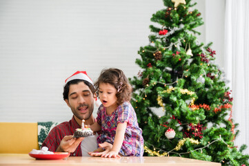 Happy family of father wear santa hat sitting on floor and hold cake birthday to surprised for cute baby daughter