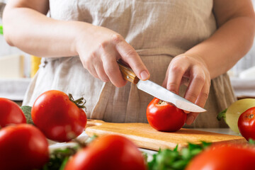 Chef slicing tomato using knife on the table in restaurant. Process of cutting and preparation food in kitchen.