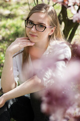 girl with glasses sitting under a blossoming tree in a park