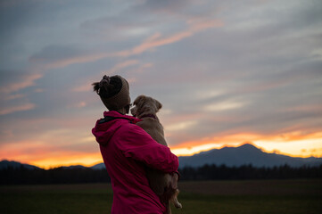 Woman holding her dog looking at beautiful sunset sky