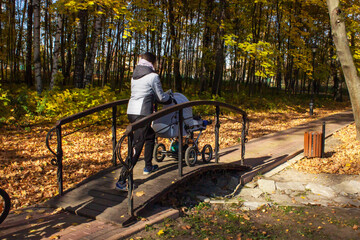 Woman in blue coat walking with baby pram in autumn park. Mother with child on a lake coast, leisure on nature