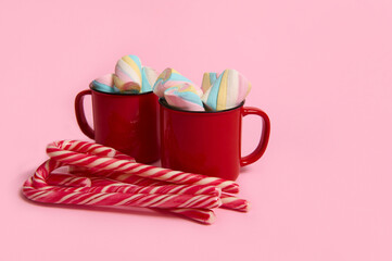 Coffee mugs with marshmallows and candy canes on pink colored background. Christmas hot drink with desserts. Hot chocolate, cup of coffee cocoa. New year, merry christmas holiday celebration