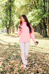 Beautiful woman drink coffee, using phone and walking in the park.
