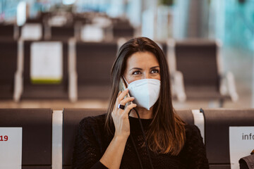 Tourist woman at the airport waiting for her flight. Wearing a mask for covid 19 protection making a call while waiting. Lifestyle. Travel