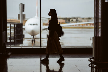 Woman silhouette at the airport waiting for her flight. Wearing a mask for covid 19 protection....