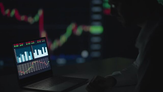 A professional with glasses looks at the computer monitor screen and thinks analyzing the securities market. Brooding puzzled broker waits for the growth of shares