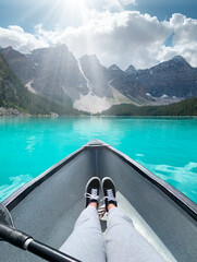 Girls legs stretched out in a canoe with turquoise lake, mountains and bright sunshine