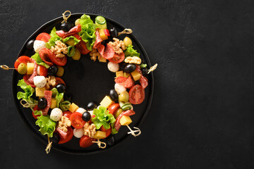 Fototapeta na wymiar Christmas food wreath of holiday snacks, canapes, tomatoes, olive, vegetables, mozzarella cheese for festive Xmas party on black background. View from above.