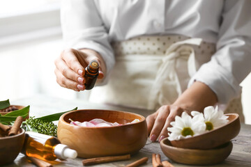 Woman adding essential oil to water in bowl on table