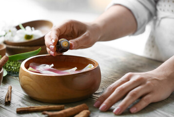 Fototapeta na wymiar Woman adding essential oil to water in bowl on table