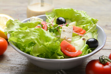 Plate with healthy salad with feta cheese and olives on wooden background