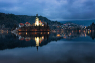 Fototapeta na wymiar A mysterious evening view of Lake Bled, Slovenia. Landscape with the lights of the city at night. Church on an island, postcard view, national park, Julian Alps.