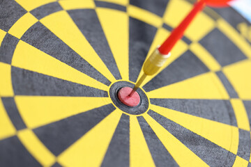 Dart in center of yellow-black dart board closeup